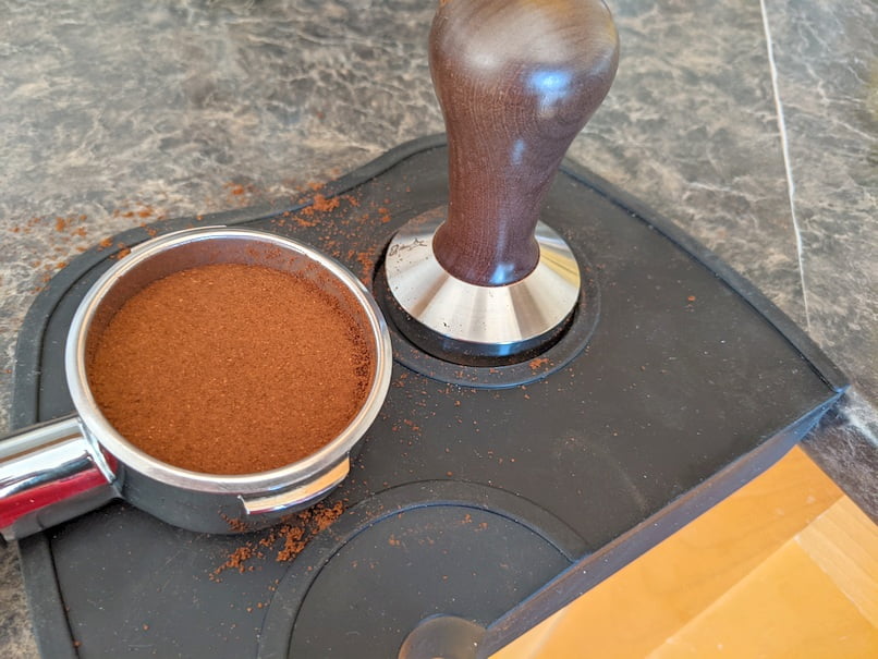 Tamped coffee in portafilter with tamper and tamping mat