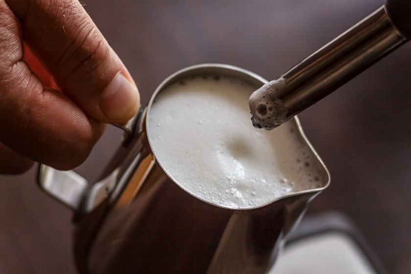 professional bartender warming milk for cappuccino. barista usin
